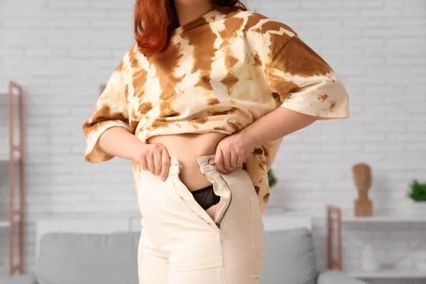 Image of woman trying to do her trousers up after pregnancy weight gain Earls Barton