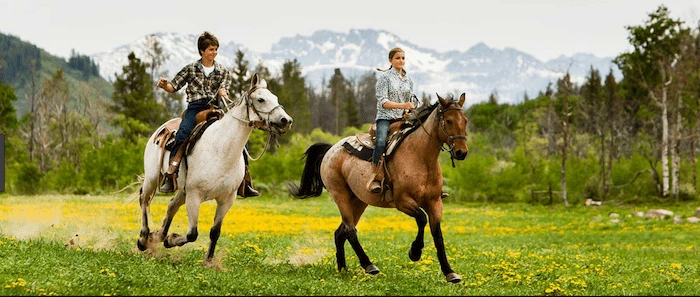 Confident plus-size woman riding Earls Barton a horse through a field with a smile on her face.